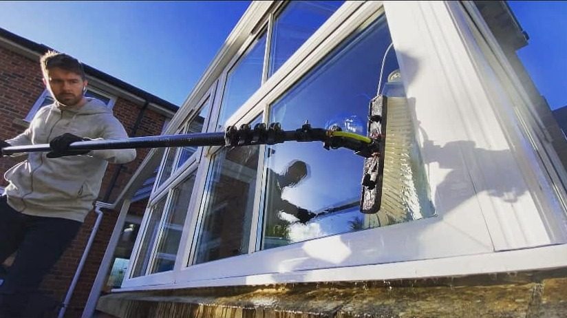 Cleaning conservatory windows with a water-fed brush on a sunny day