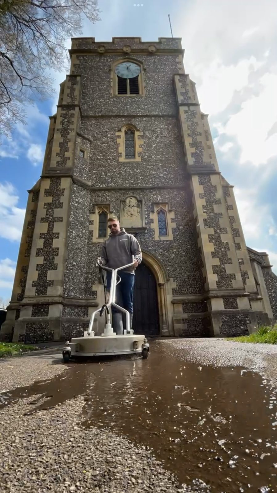 Rotary surface cleaner at work on the forecourt in front of a flint church tower